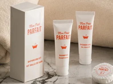Kit salle de bain : boîte, shampoing, gel douche et savon posés devant des serviettes roulées